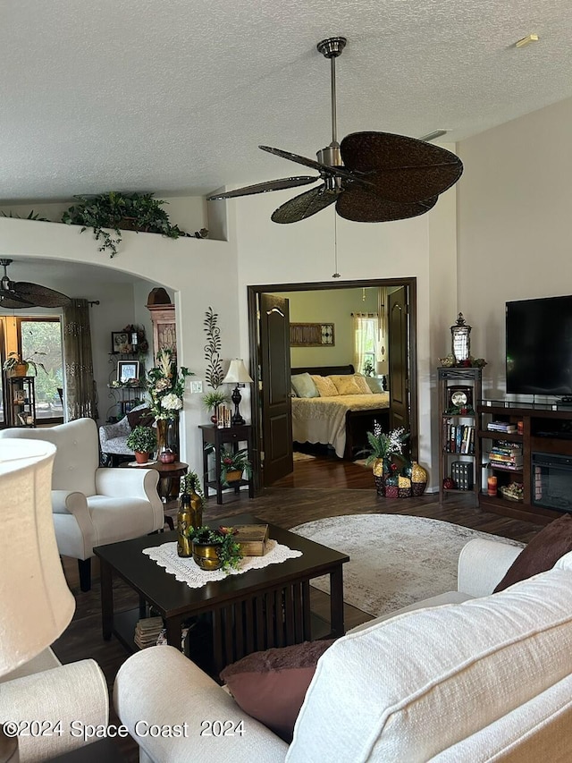 living room with a textured ceiling, ceiling fan, dark wood-type flooring, and vaulted ceiling