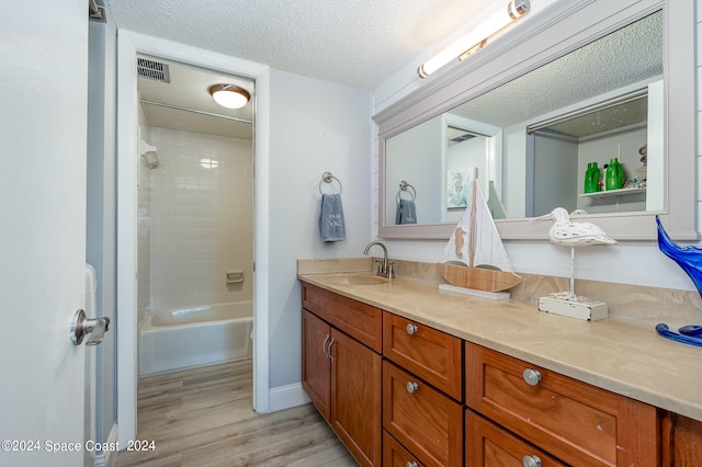 bathroom with a textured ceiling, wood-type flooring, vanity, and tiled shower / bath