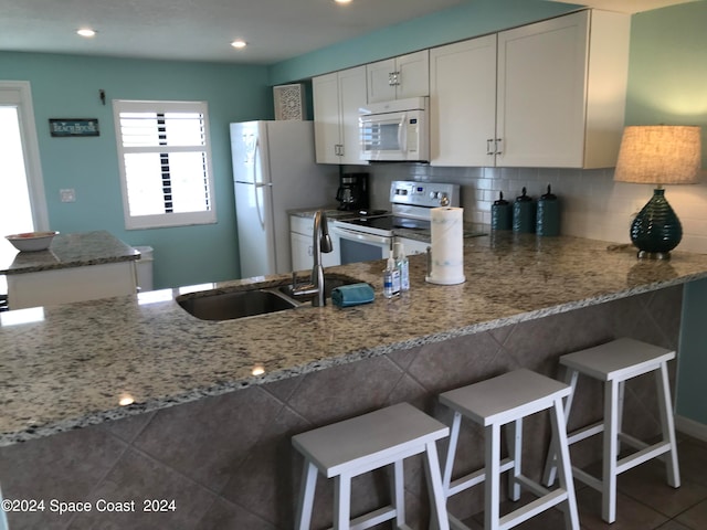 kitchen with sink, white cabinets, kitchen peninsula, white appliances, and light stone countertops