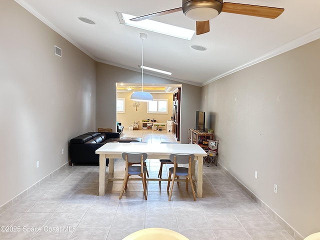 dining room with lofted ceiling with skylight, light tile patterned flooring, crown molding, and a ceiling fan