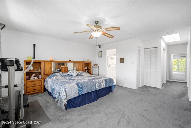 carpeted bedroom with a textured ceiling, connected bathroom, ceiling fan, and a skylight