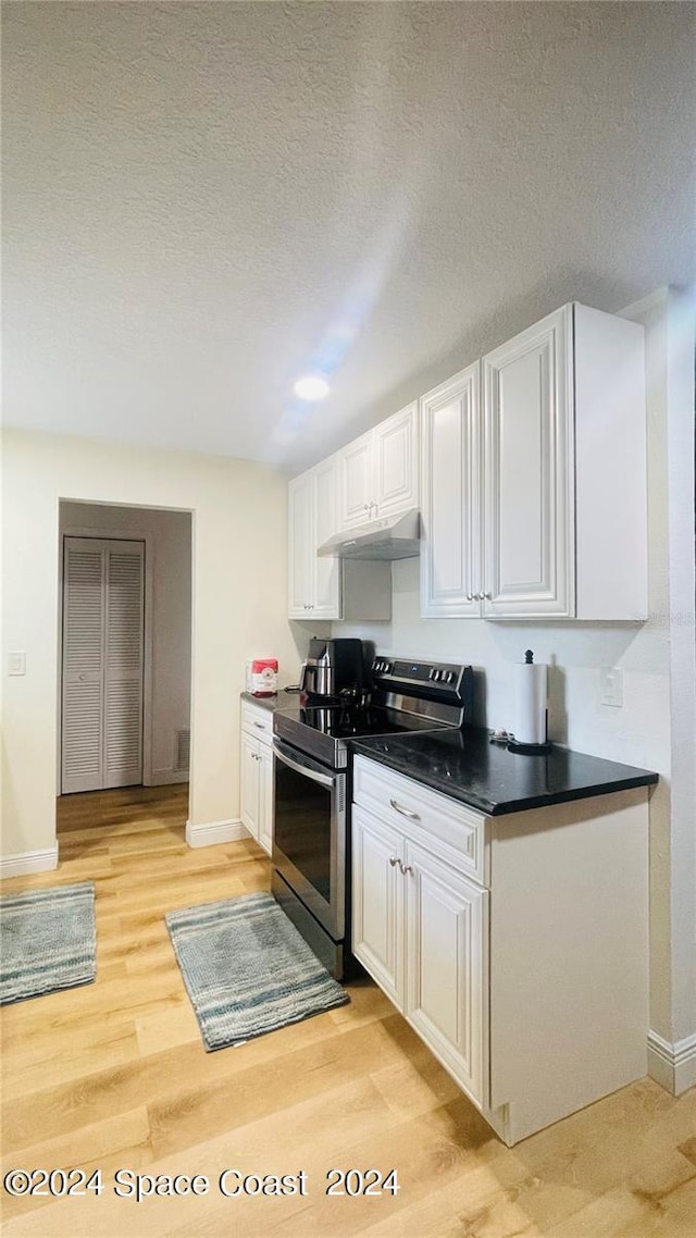 kitchen featuring white cabinets, stainless steel electric stove, light wood-type flooring, and a textured ceiling