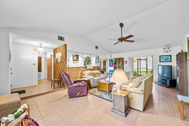 tiled living room with lofted ceiling, wood walls, ceiling fan, and a textured ceiling