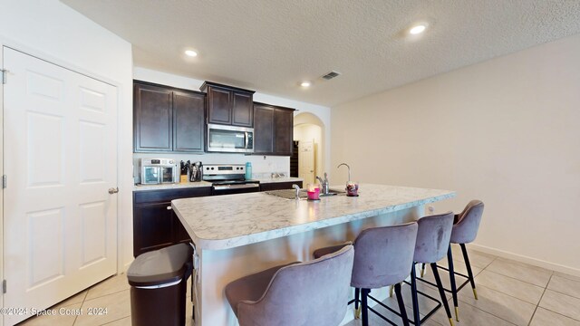 kitchen with appliances with stainless steel finishes, a kitchen island with sink, a kitchen bar, and a textured ceiling