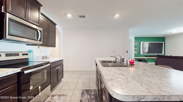 kitchen with appliances with stainless steel finishes, a textured ceiling, sink, and an island with sink