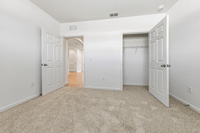 unfurnished bedroom with a textured ceiling, a closet, and light carpet