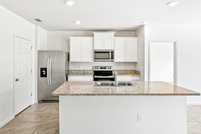 kitchen with white cabinets, appliances with stainless steel finishes, light stone countertops, an island with sink, and a textured ceiling