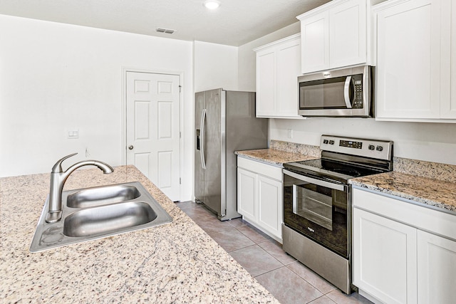 kitchen featuring light tile patterned floors, stainless steel appliances, sink, light stone counters, and white cabinets