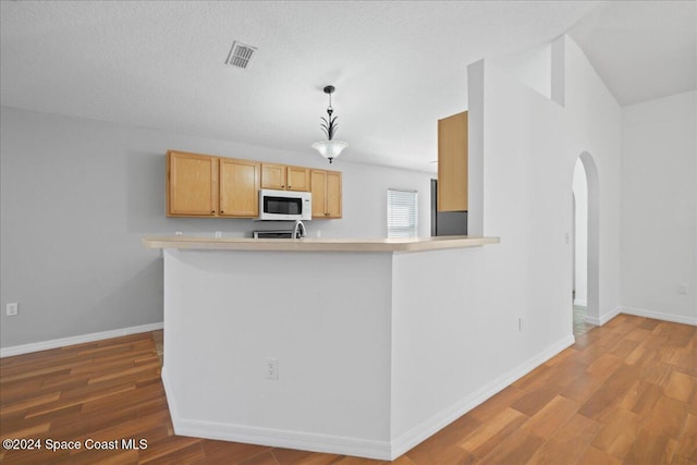 kitchen featuring hardwood / wood-style flooring, decorative light fixtures, kitchen peninsula, and light brown cabinetry