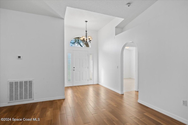 entryway featuring a notable chandelier, a towering ceiling, a textured ceiling, and hardwood / wood-style flooring