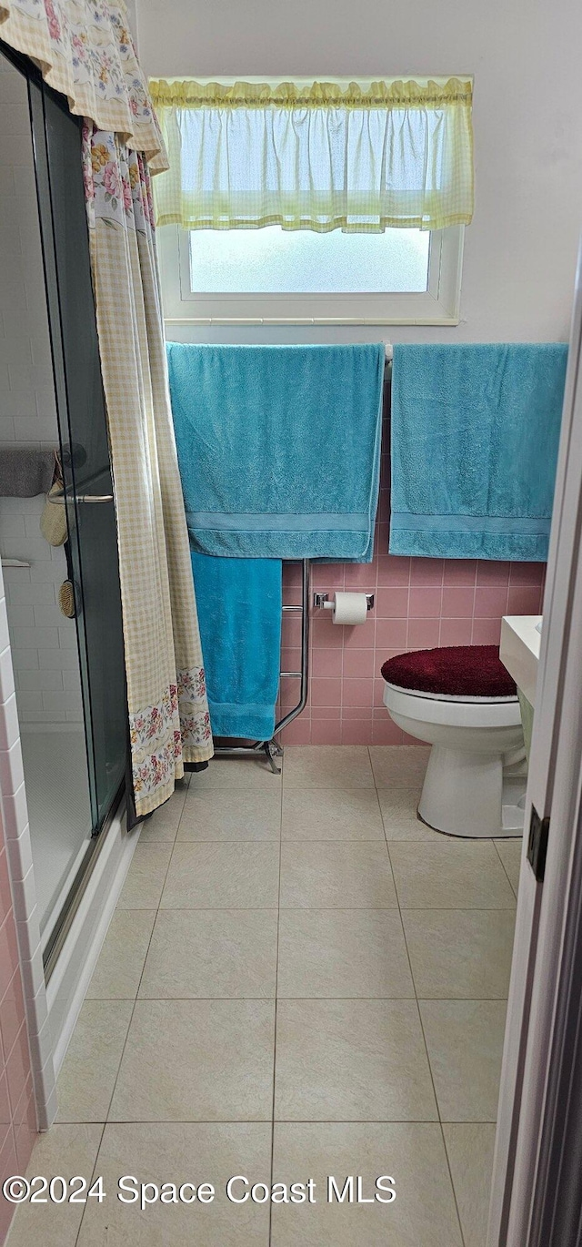 bathroom featuring tile patterned floors, a shower with shower door, tile walls, and a wealth of natural light