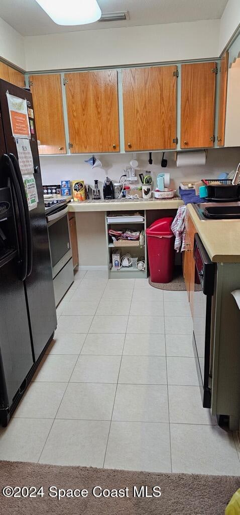 kitchen with black fridge with ice dispenser, light tile patterned floors, and electric stove