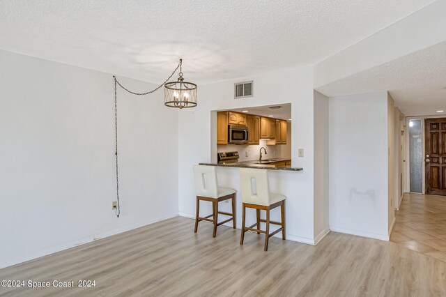 kitchen with kitchen peninsula, pendant lighting, light wood-type flooring, a textured ceiling, and sink