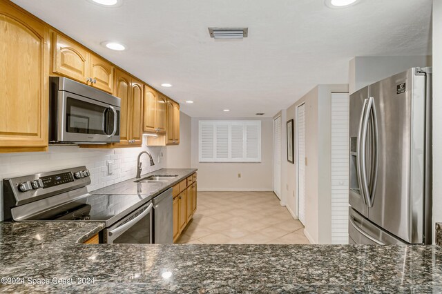 kitchen with appliances with stainless steel finishes, sink, dark stone counters, and tasteful backsplash