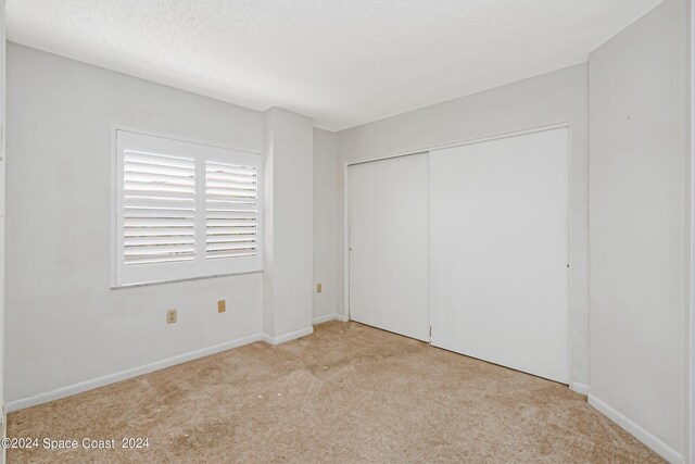 unfurnished bedroom featuring a textured ceiling, light colored carpet, and a closet