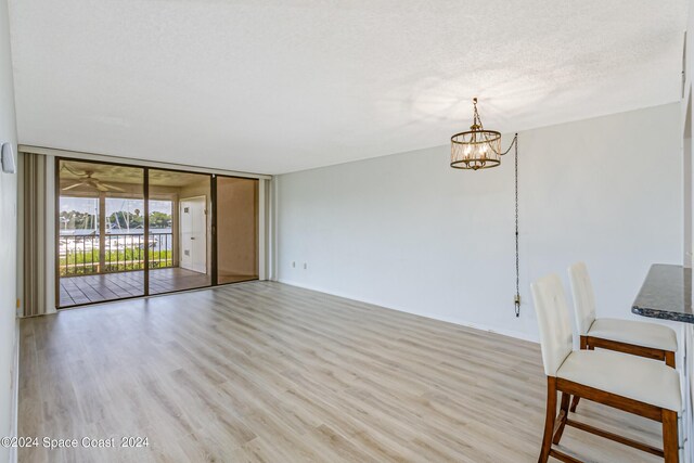 interior space featuring light wood-type flooring, a chandelier, a textured ceiling, and expansive windows