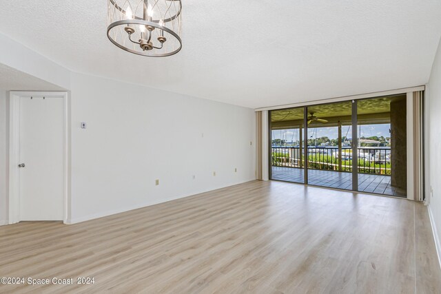 unfurnished room featuring light hardwood / wood-style flooring, a chandelier, a textured ceiling, and a wall of windows