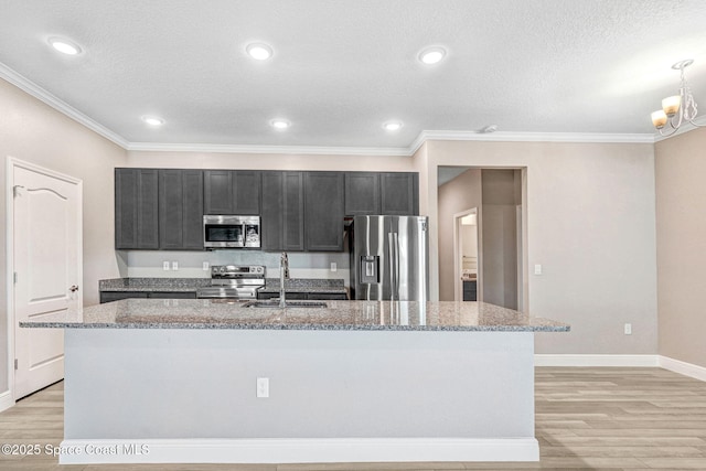 kitchen featuring sink, stainless steel appliances, light stone counters, an island with sink, and light wood-type flooring