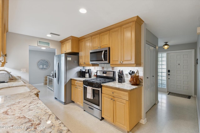 kitchen with appliances with stainless steel finishes, light stone counters, tasteful backsplash, light brown cabinetry, and sink