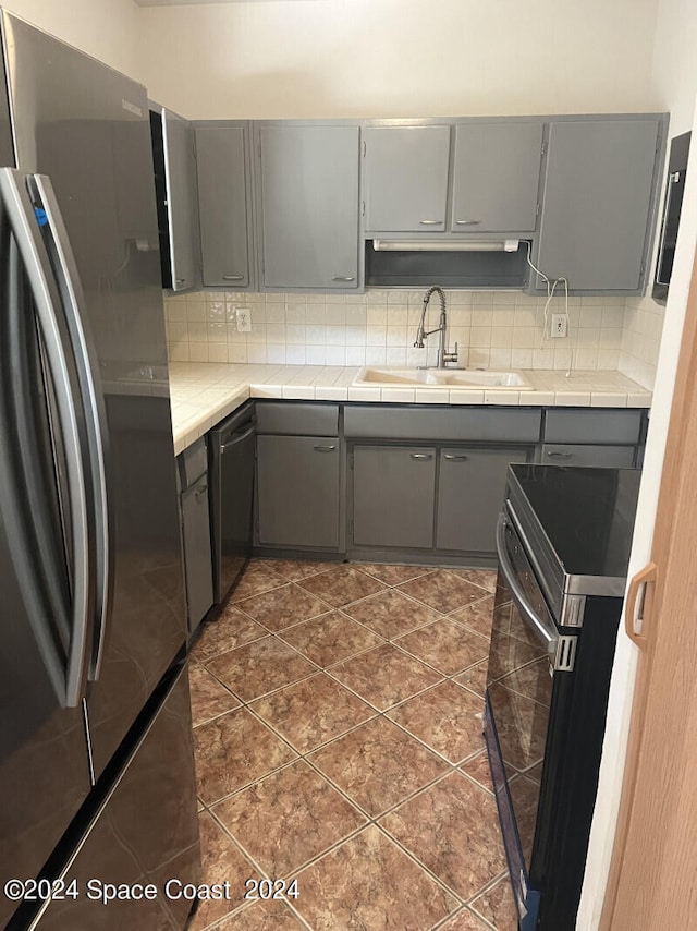 kitchen featuring dark tile patterned flooring, sink, gray cabinetry, stainless steel appliances, and decorative backsplash