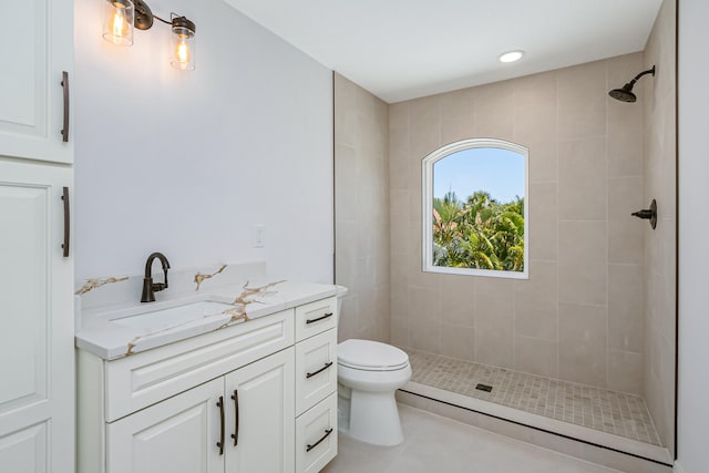 bathroom with a tile shower, vanity, tile patterned flooring, and toilet