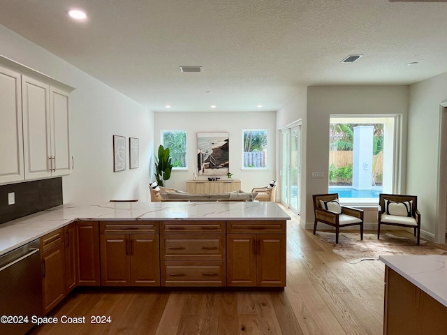 kitchen with light stone counters, kitchen peninsula, a textured ceiling, dishwasher, and light wood-type flooring