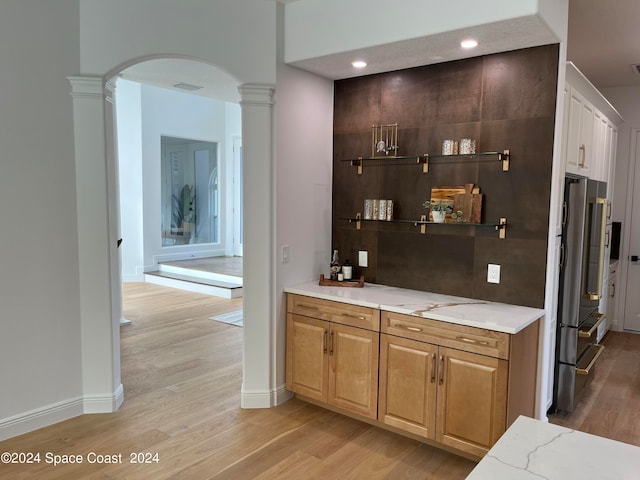 bar featuring light wood-type flooring, light stone counters, decorative columns, and high end fridge