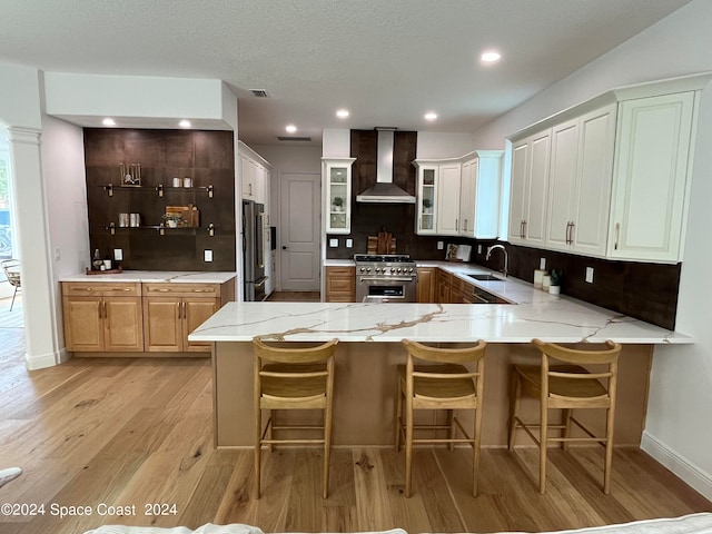 kitchen with kitchen peninsula, light hardwood / wood-style flooring, wall chimney range hood, white cabinetry, and high quality appliances