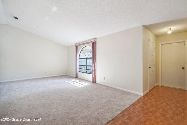 carpeted spare room with a textured ceiling and vaulted ceiling