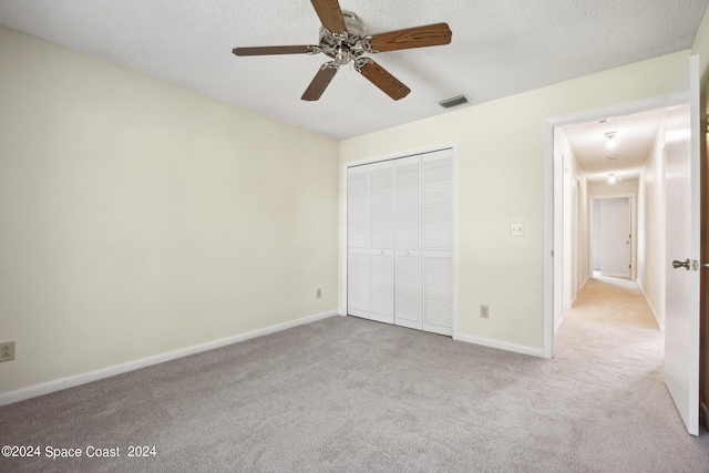 unfurnished bedroom featuring a closet, ceiling fan, light colored carpet, and a textured ceiling