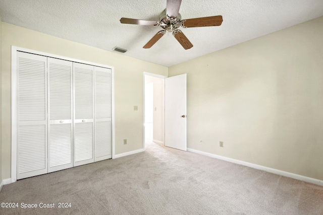 unfurnished bedroom featuring ceiling fan, light colored carpet, a textured ceiling, and a closet