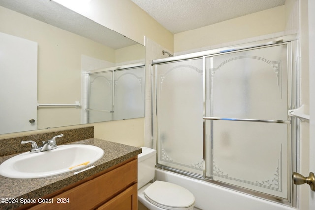 full bathroom with a textured ceiling, bath / shower combo with glass door, vanity, and toilet