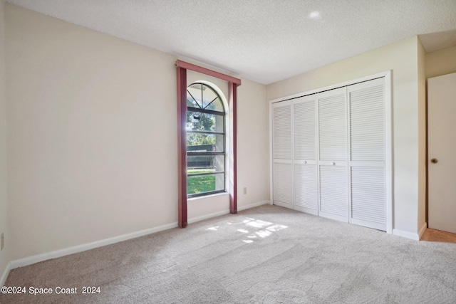 unfurnished bedroom with a textured ceiling, light colored carpet, and a closet