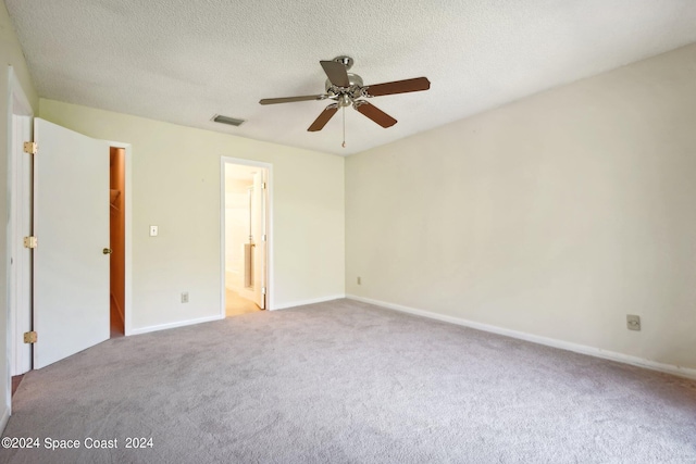 unfurnished bedroom featuring connected bathroom, a textured ceiling, ceiling fan, a walk in closet, and light carpet