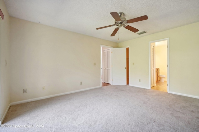 unfurnished bedroom featuring ceiling fan, light colored carpet, ensuite bathroom, and a textured ceiling