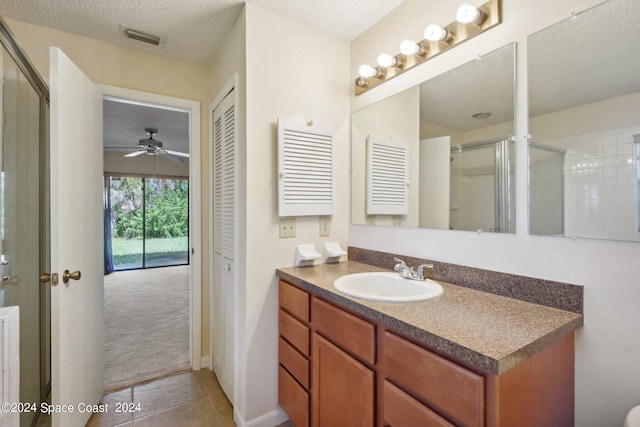 bathroom with ceiling fan, vanity, a textured ceiling, a shower with shower door, and tile patterned flooring