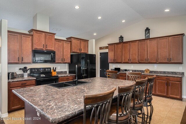 kitchen featuring a textured ceiling, a kitchen island with sink, black appliances, a breakfast bar, and vaulted ceiling