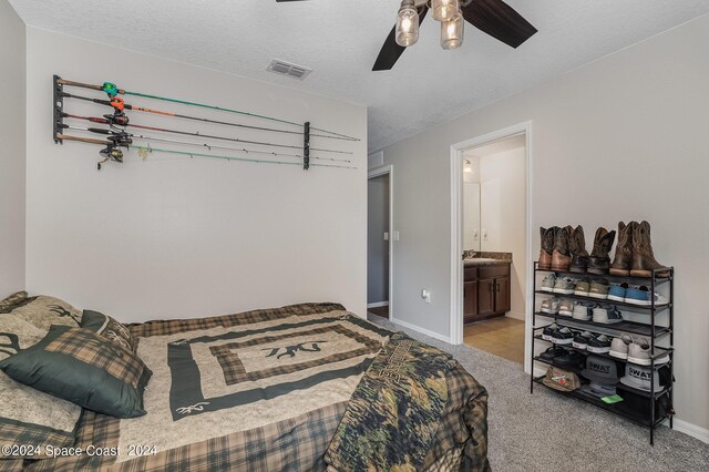 bedroom featuring ceiling fan, light colored carpet, a textured ceiling, and ensuite bath