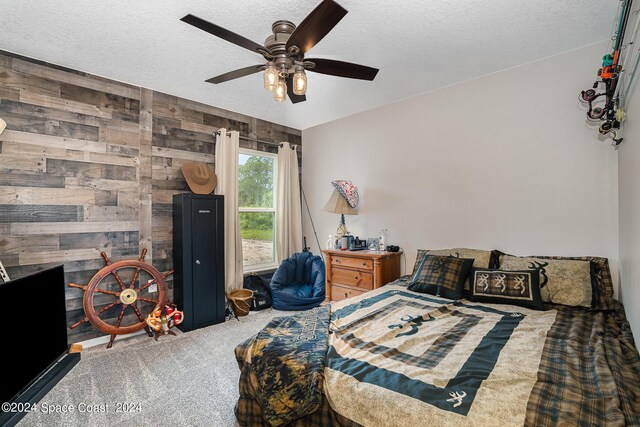 carpeted bedroom with a textured ceiling, wood walls, and ceiling fan