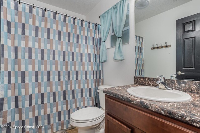 bathroom featuring a textured ceiling, vanity, toilet, and walk in shower