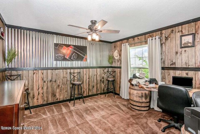 carpeted office featuring ornamental molding, wood walls, ceiling fan, and a textured ceiling