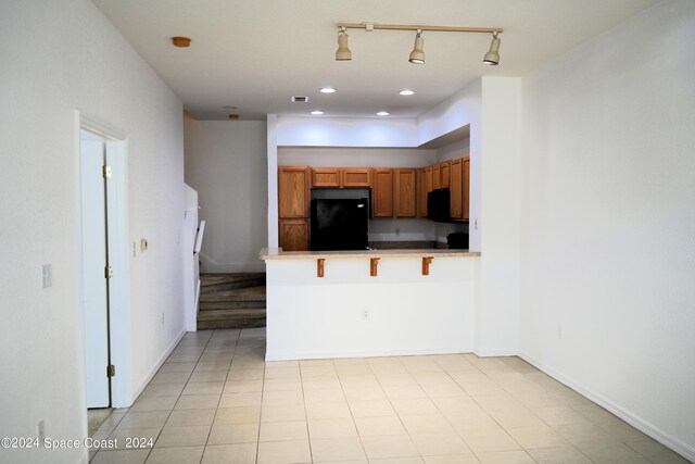 kitchen featuring light tile patterned floors, a breakfast bar, kitchen peninsula, and black appliances