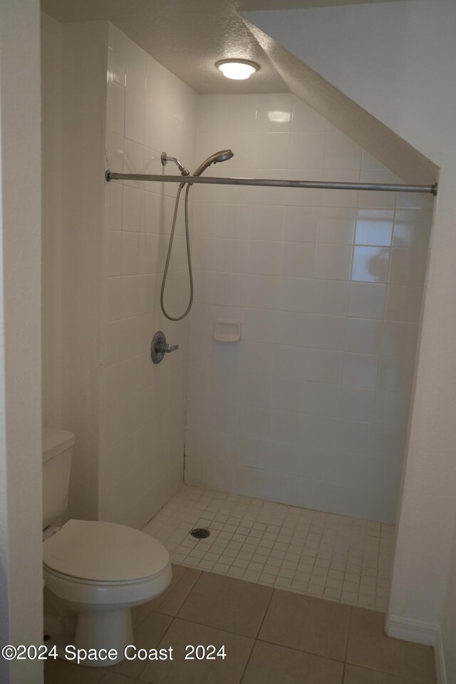 bathroom featuring a textured ceiling, tile patterned flooring, toilet, and tiled shower