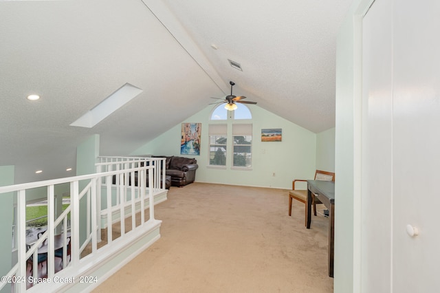 additional living space with light carpet, a textured ceiling, vaulted ceiling with skylight, and ceiling fan