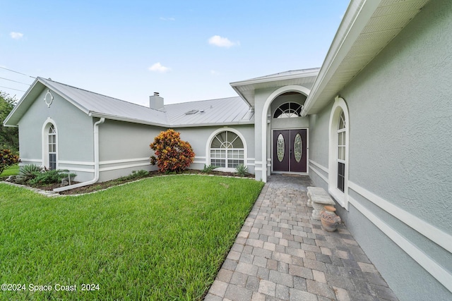 doorway to property featuring a chimney, metal roof, stucco siding, and a lawn