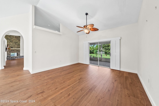 spare room with a stone fireplace, hardwood / wood-style floors, ceiling fan, and high vaulted ceiling