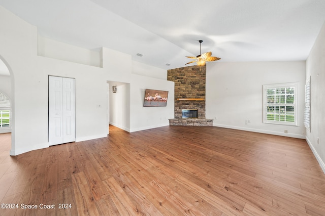 unfurnished living room featuring ceiling fan, a stone fireplace, lofted ceiling, and light wood-type flooring