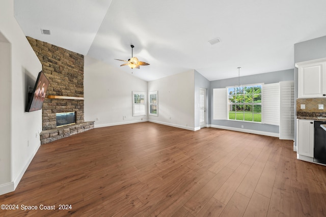 unfurnished living room with a stone fireplace, lofted ceiling, ceiling fan, and hardwood / wood-style flooring