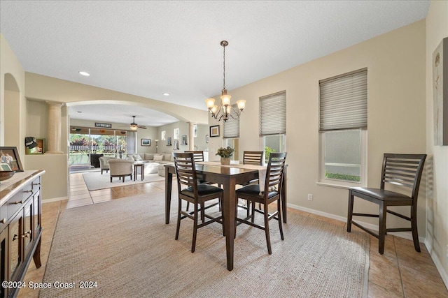 tiled dining room with a textured ceiling, ceiling fan with notable chandelier, and decorative columns