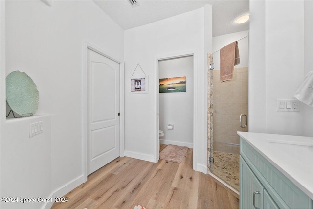 bathroom with vanity, a textured ceiling, toilet, a shower with door, and hardwood / wood-style floors